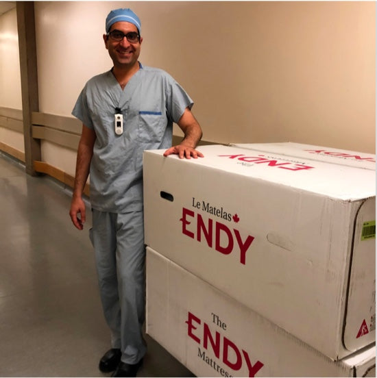 Une travailleuse de la santé de l'hôpital pour femmes de la Colombie-Britannique portant des gommages et posant avec une boîte de matelas Endy.