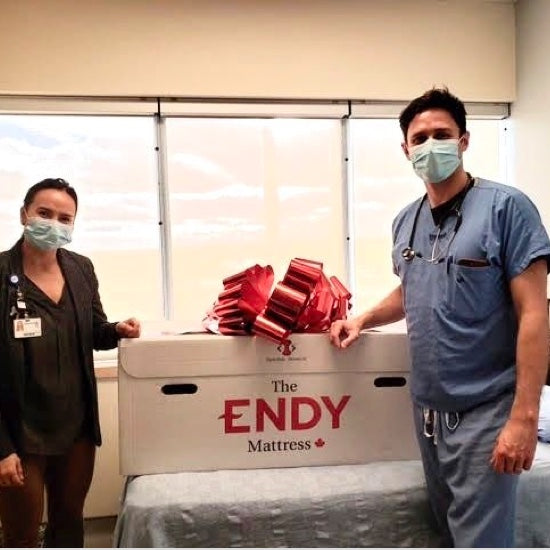 Deux travailleurs de la santé de l'hôpital de Southlake portant des gommages et posant avec une boîte de matelas Endy.